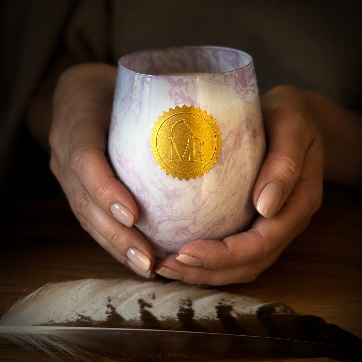 Hands holding a luxury pink and white marbled glass candle with a gold MR seal, showcasing an elegant handmade scented candle by Miss Rio.