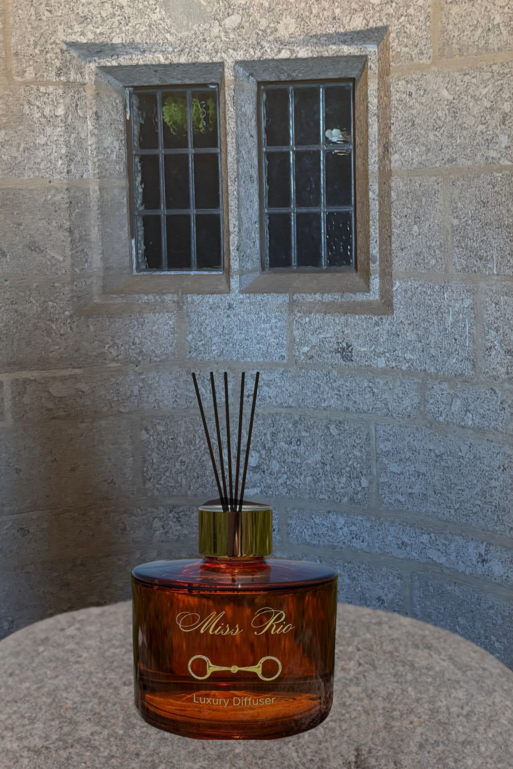 Reed diffuser labeled 'Miss Rio' on a stone surface with a stone wall background
