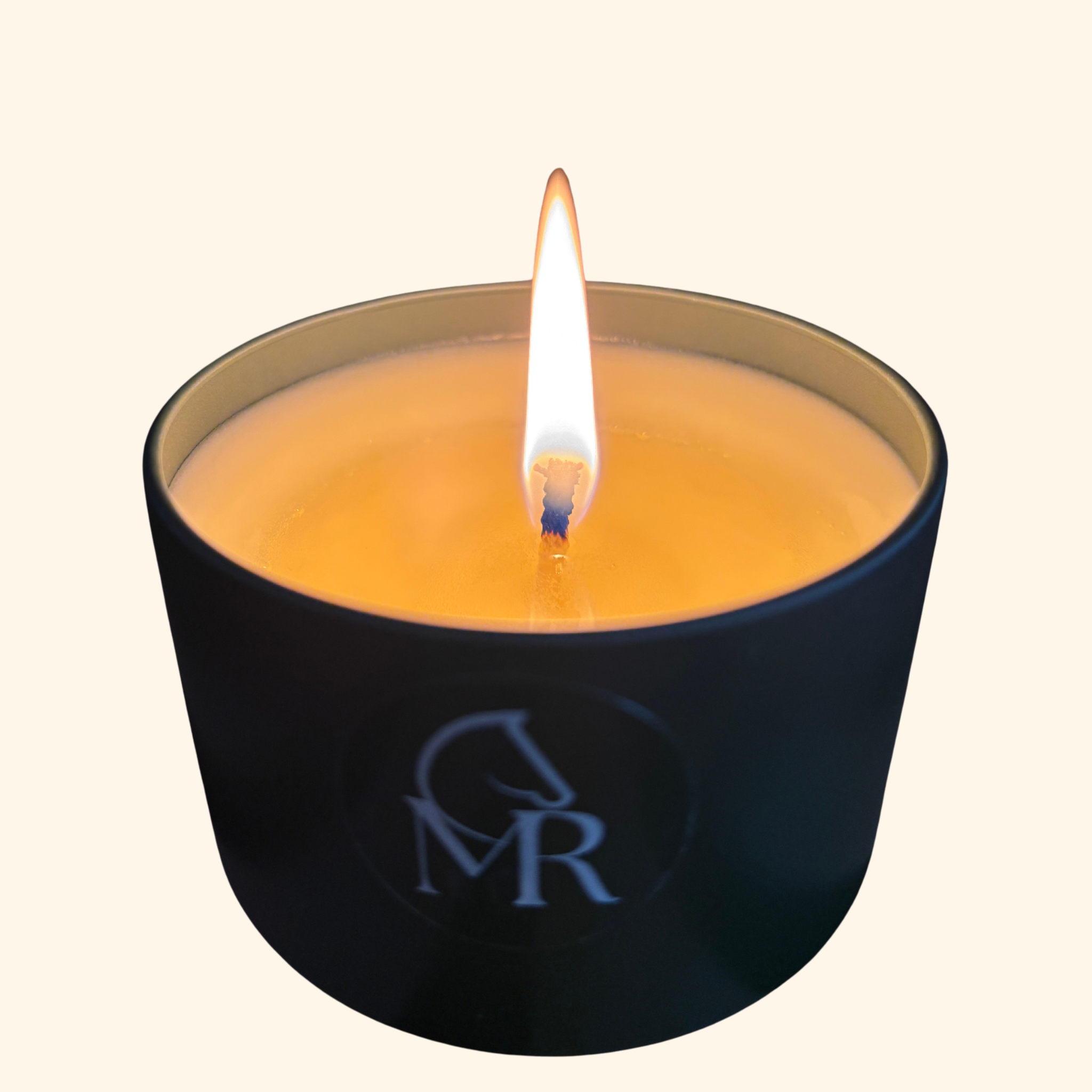 Close-up of a lit Miss Rio Leather & Tack candle in a matte black travel tin with CMR monogram, golden wax pool glowing against a cream background.