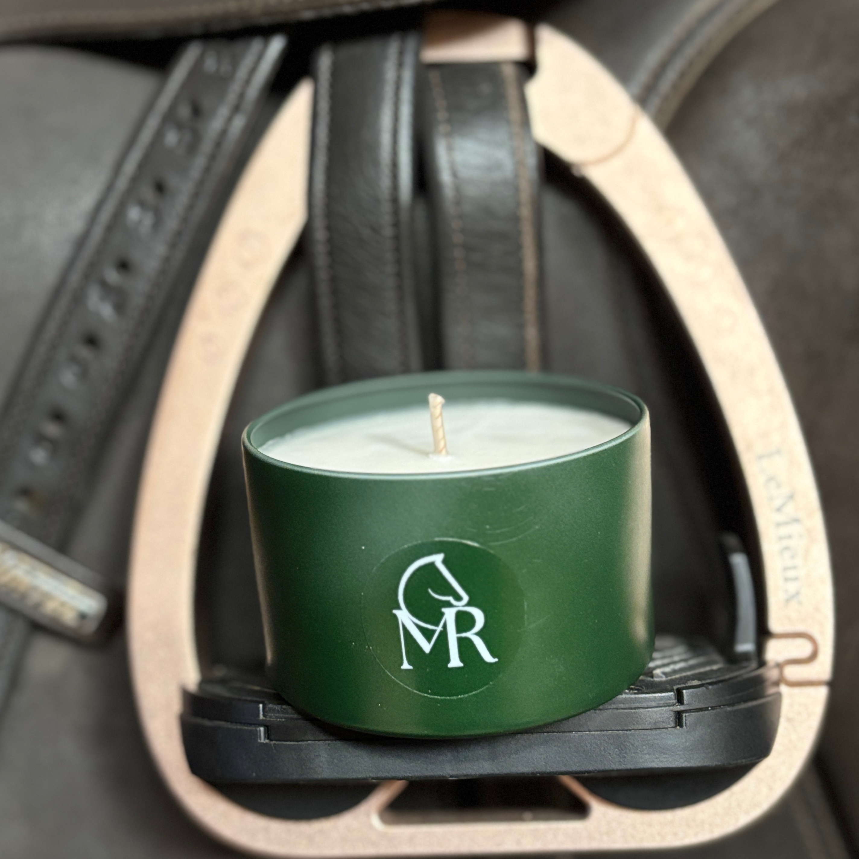 Miss Rio luxury soy candle in a green travel tin with MR equestrian logo, sitting inside a stirrup iron on a dark leather saddle. The perfect equestrian home fragrance, hand-poured in Devon. Tomato Vine scent.